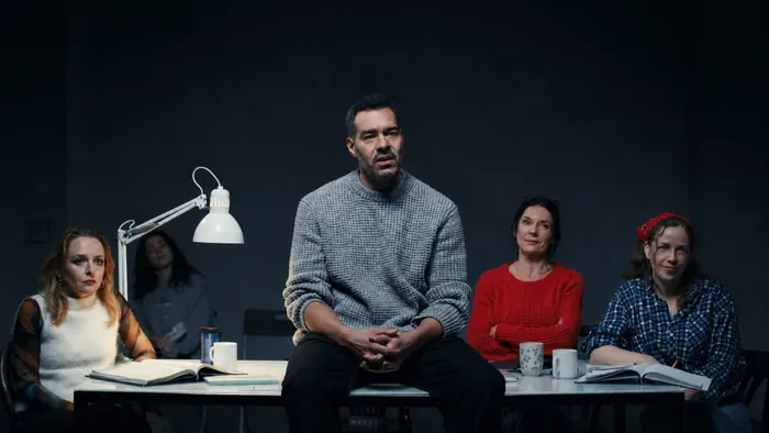 Szene aus „Die Ideen“: Ein Mann im grauen Pullover sitzt vorn auf einem Tisch, um ihn herum vier Frauen mit Büchern und Tassen, daneben eine weiße Schreibtischlampe