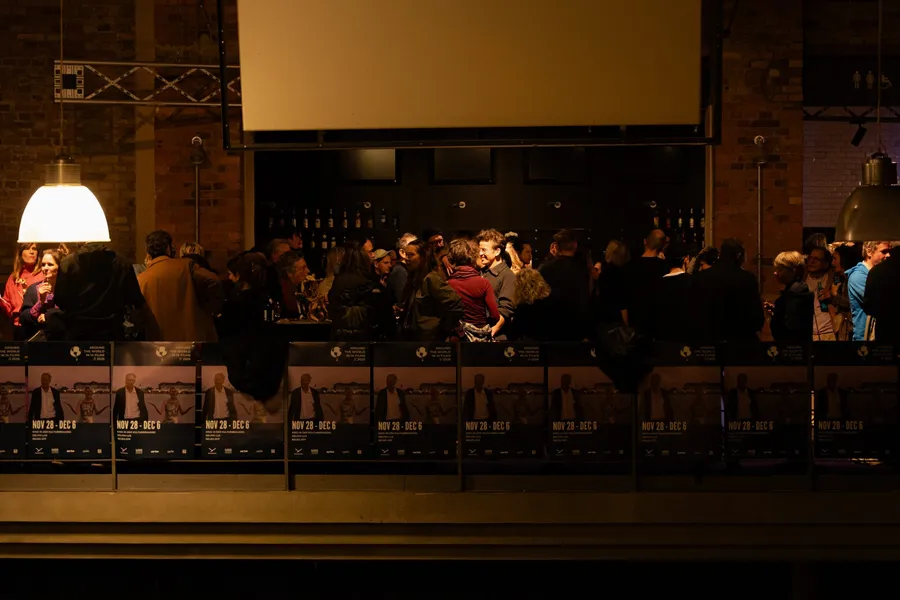The foyer in the evening, guests at the bar, a row of festival posters along the balustrade