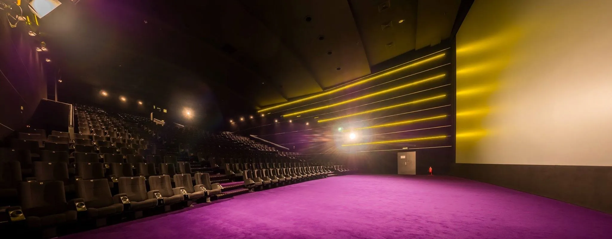 Leerer Saal mit violettem Teppich und gelben Lichtbändern an der Wand