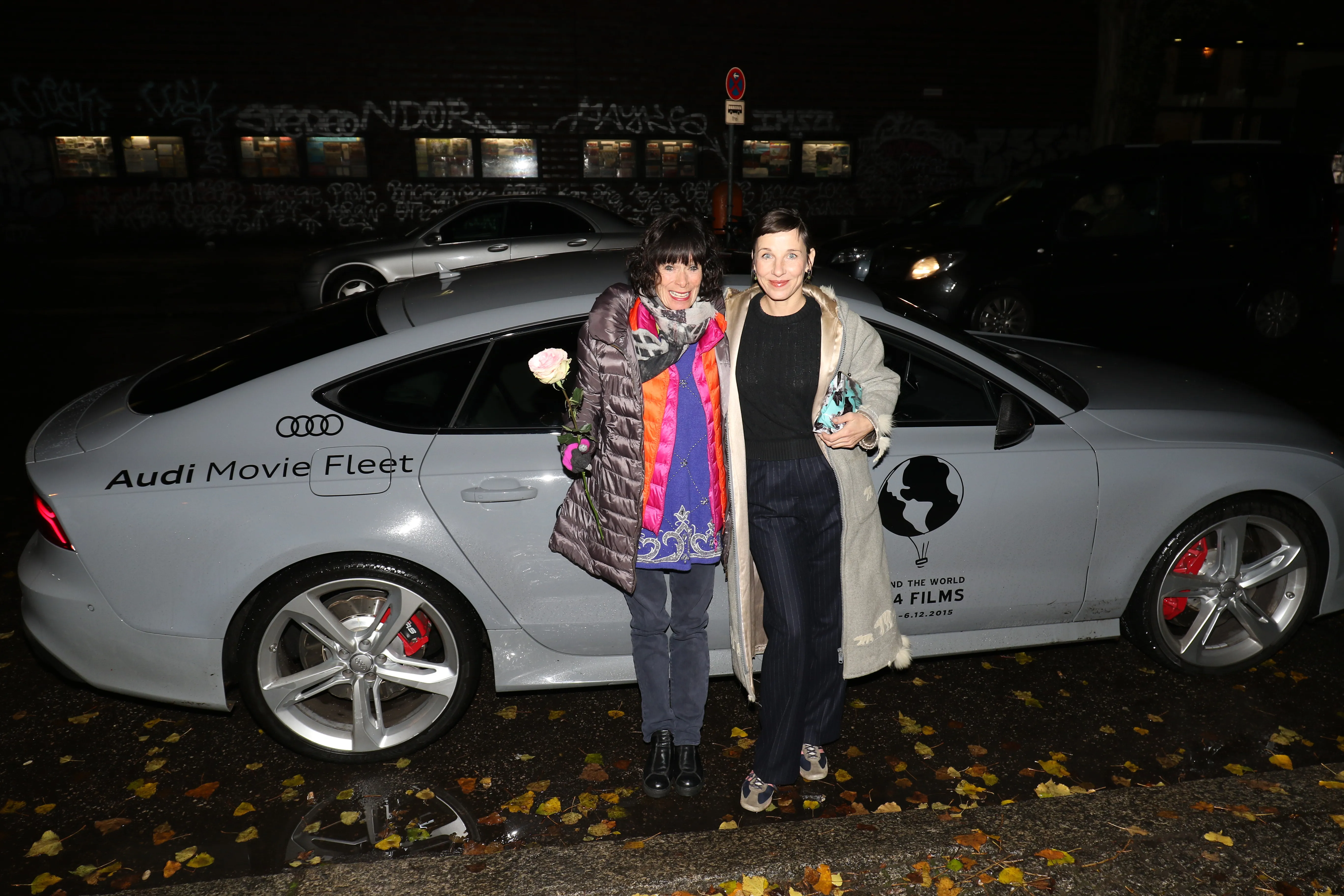 Zwei Personen stehen nachts vor einem Wagen der Audi Movie Fleet mit dem Festivallogo auf der Tür.