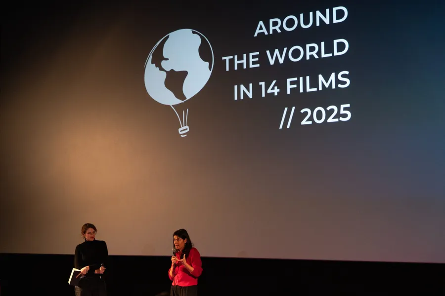 Two women on stage in front of the screen, one speaking into a microphone, the festival logo behind them